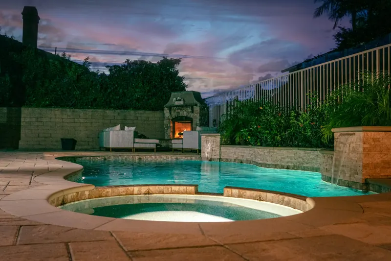 Example of a lit backyard pool and spa at dusk